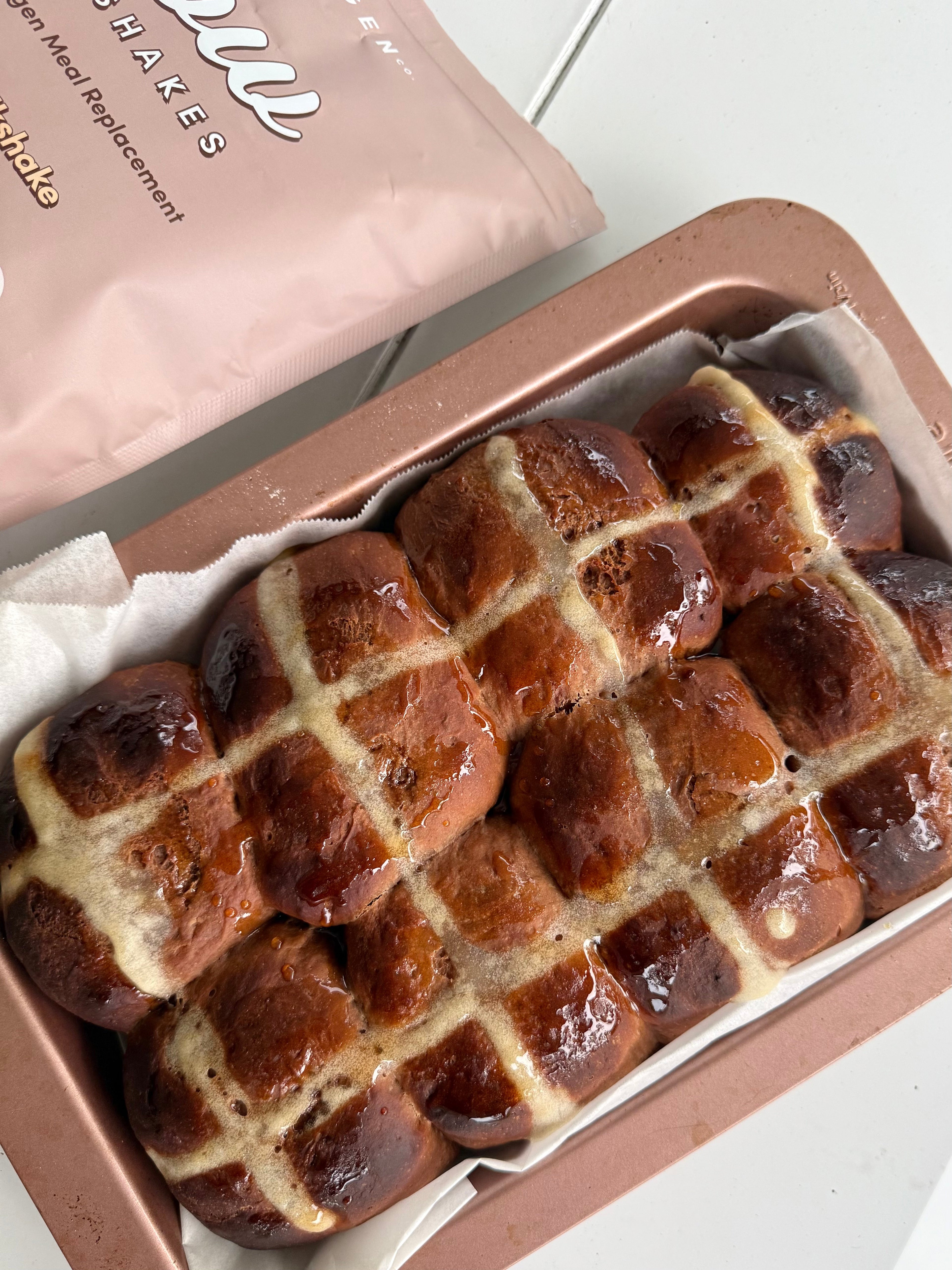 Freshly baked hot cross buns with white crosses on top, arranged on a baking tray.