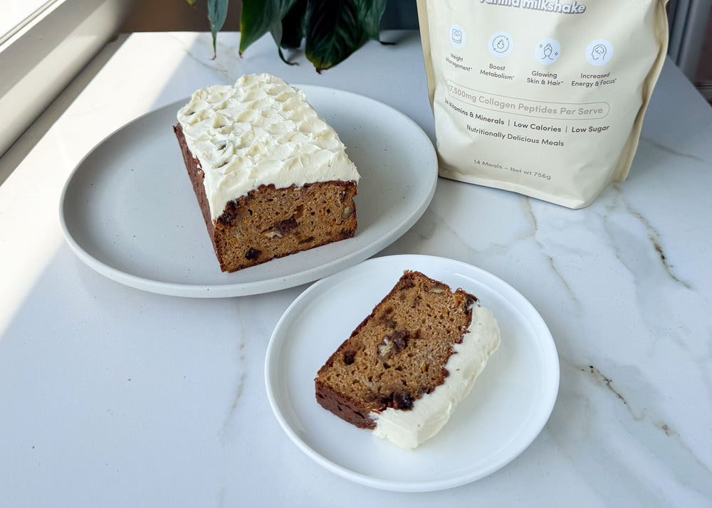 Slice of frosted loaf cake on a plate with the remaining loaf and protein powder in the background.