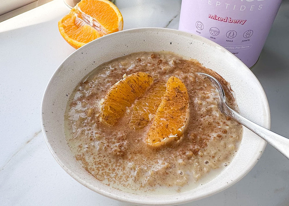 Bowl of creamy brown rice pudding topped with orange segments and a sprinkle of cinnamon, with a spoon and sliced orange on the side.